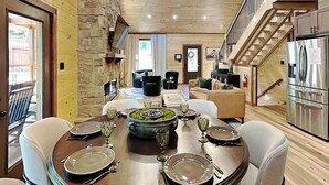 A dining area with a wooden table set for six, a stone fireplace, and a kitchen with a stainless steel refrigerator. - Mountain Ventures by Jackson Mountain Rentals (Pigeon Forge)