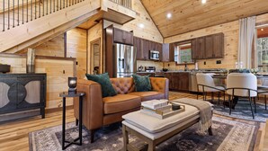 A spacious cabin interior with a loft bedroom, a cozy living area with a sofa and coffee table, a kitchen with modern appliances, and a dining area. - Mountain Ventures by Jackson Mountain Rentals (Pigeon Forge)