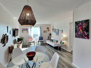 A modern living room with a glass dining table, white sofas, and a large hanging light fixture. - Let's Flamingle by Silver Sands Vacation Rentals (Port Aransas)