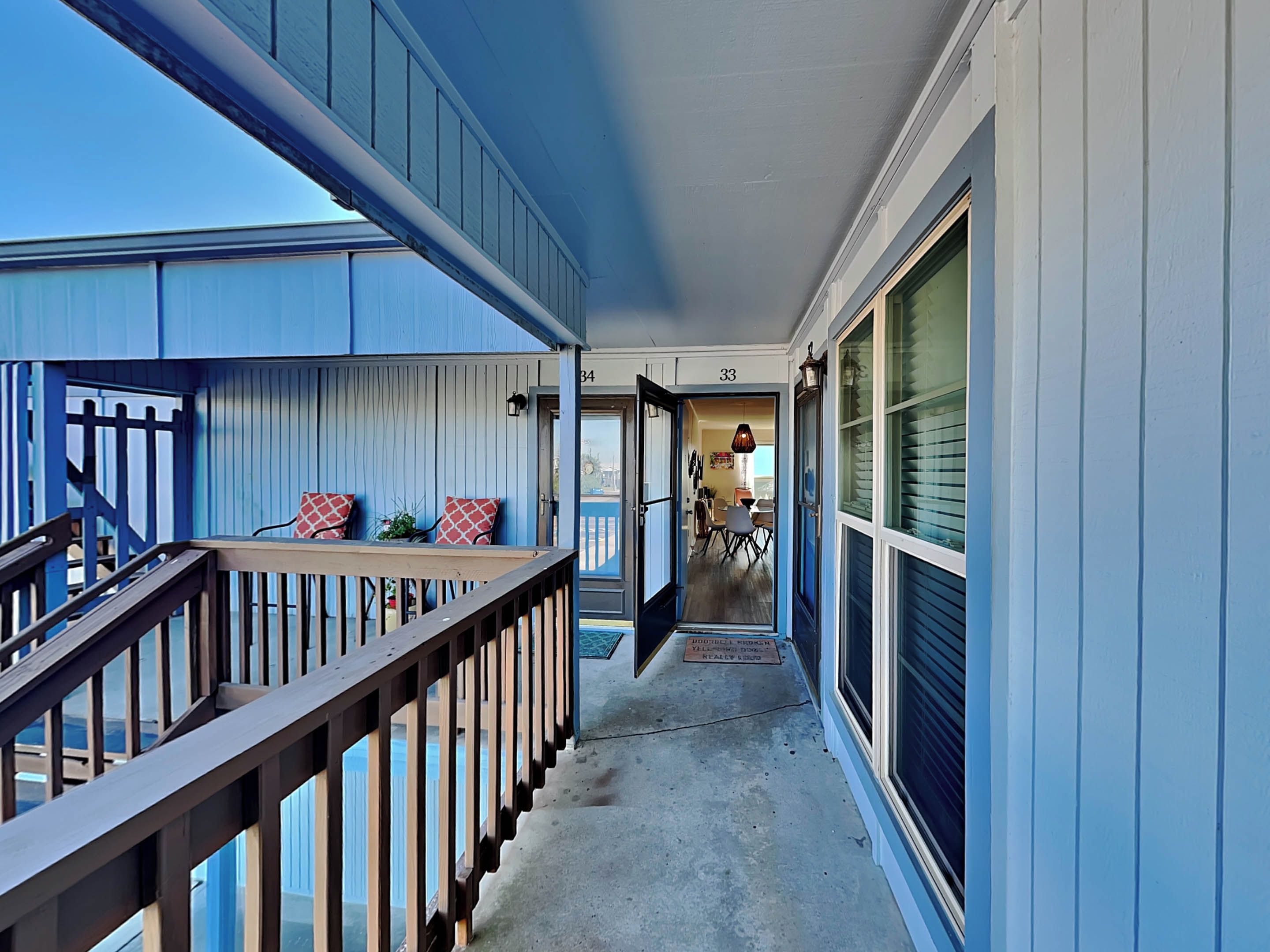 A narrow corridor with a wooden railing, a door leading to a dining area, and a view of the outside.