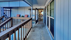 A narrow corridor with a wooden railing, a door leading to a dining area, and a view of the outside. - Let's Flamingle by Silver Sands Vacation Rentals (Port Aransas)