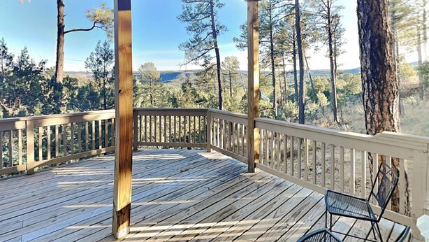 A wooden deck with a railing, a bench, and a view of a forest and hills. - Ponderosa Paradise by Ruidoso Vacation Rentals (Ruidoso)
