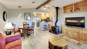 A modern living room with a sofa, a wooden coffee table, and a TV. There is a kitchen area with wooden cabinets and a stove. - Ponderosa Paradise by Ruidoso Vacation Rentals (Ruidoso)