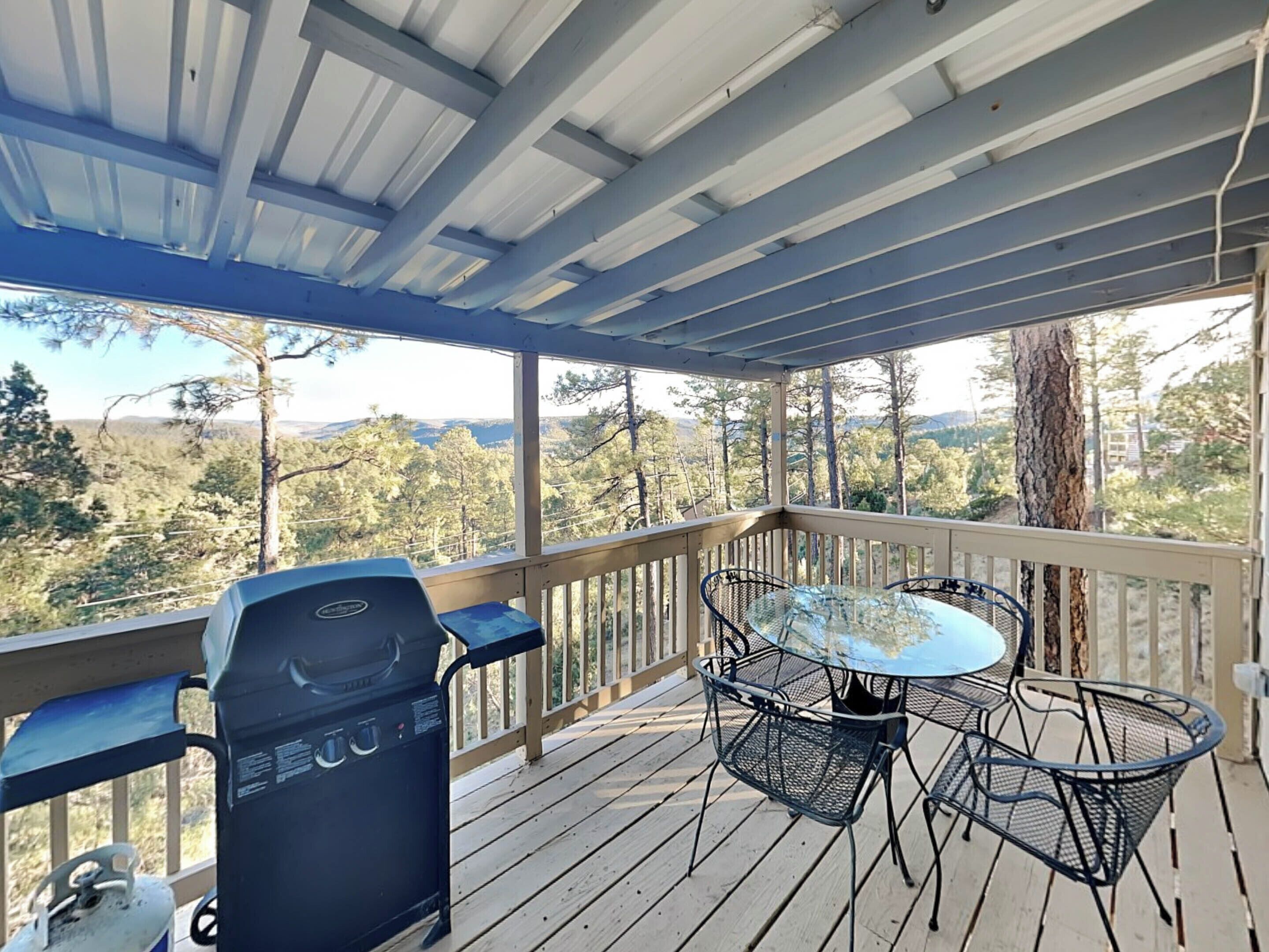 A covered outdoor deck with a grill, a table, and chairs.
