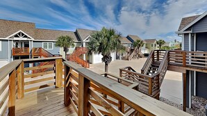 A wooden deck with a view of beach houses and palm trees. - Beach Place by Silver Sands Vacation Rentals (Port Aransas)