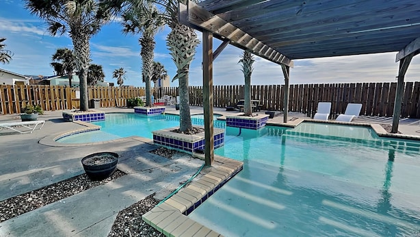 Ein Pool mit Holzterrasse, Liegestühlen und Palmen.