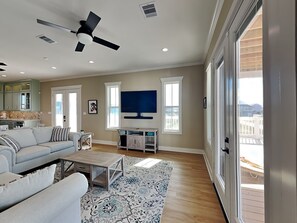 A spacious living room with a ceiling fan, a flat-screen TV, a sofa, a coffee table, and a patterned rug. - Pescador's Paradise by Ryson Vacation Rentals (Galveston)