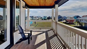 Un porche cubierto con techo de madera, una sola silla negra y vistas a una zona residencial con casas.