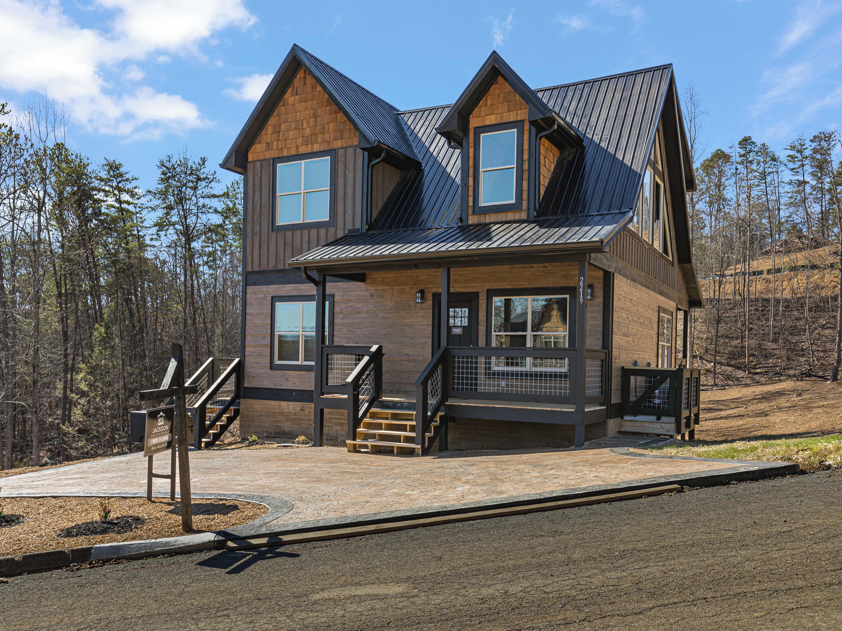A two-story log cabin with a metal roof, a front porch, and a staircase leading to the entrance.