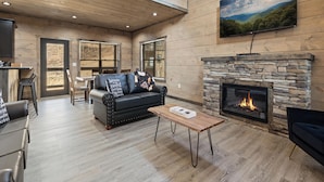 A spacious living area with a fireplace, a black leather sofa, and a wooden coffee table. - S'more Splashing by Smoky Cove Resort (Sevierville)