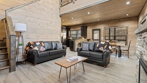 A spacious living area with a high ceiling, wooden floors, and a cozy fireplace. There is a staircase leading to an upper level, and a dining area with a table and chairs. - S'more Splashing by Smoky Cove Resort (Sevierville)