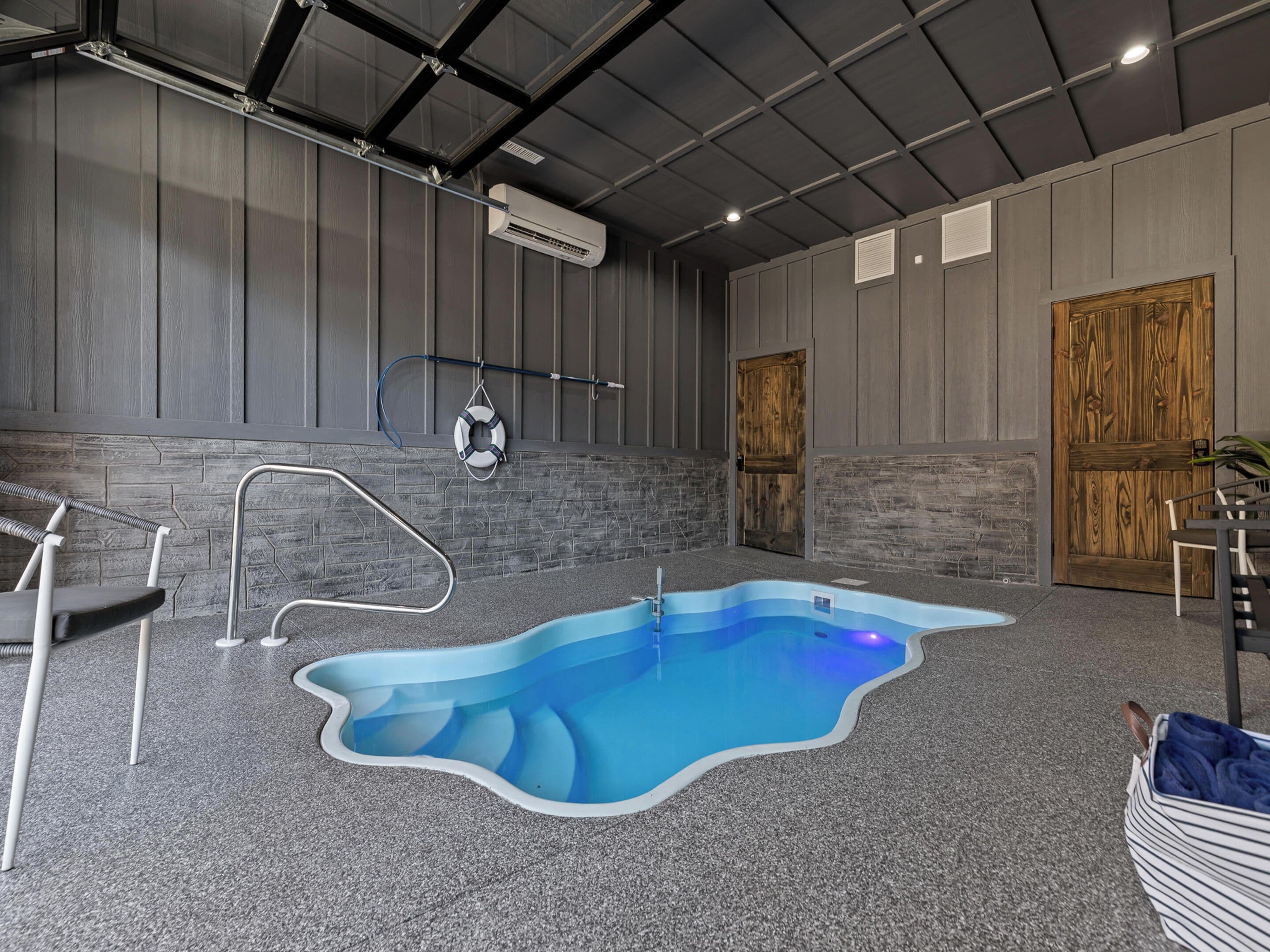 An indoor swimming pool with a unique wavy edge design, surrounded by a grey speckled floor and stone wall accents.