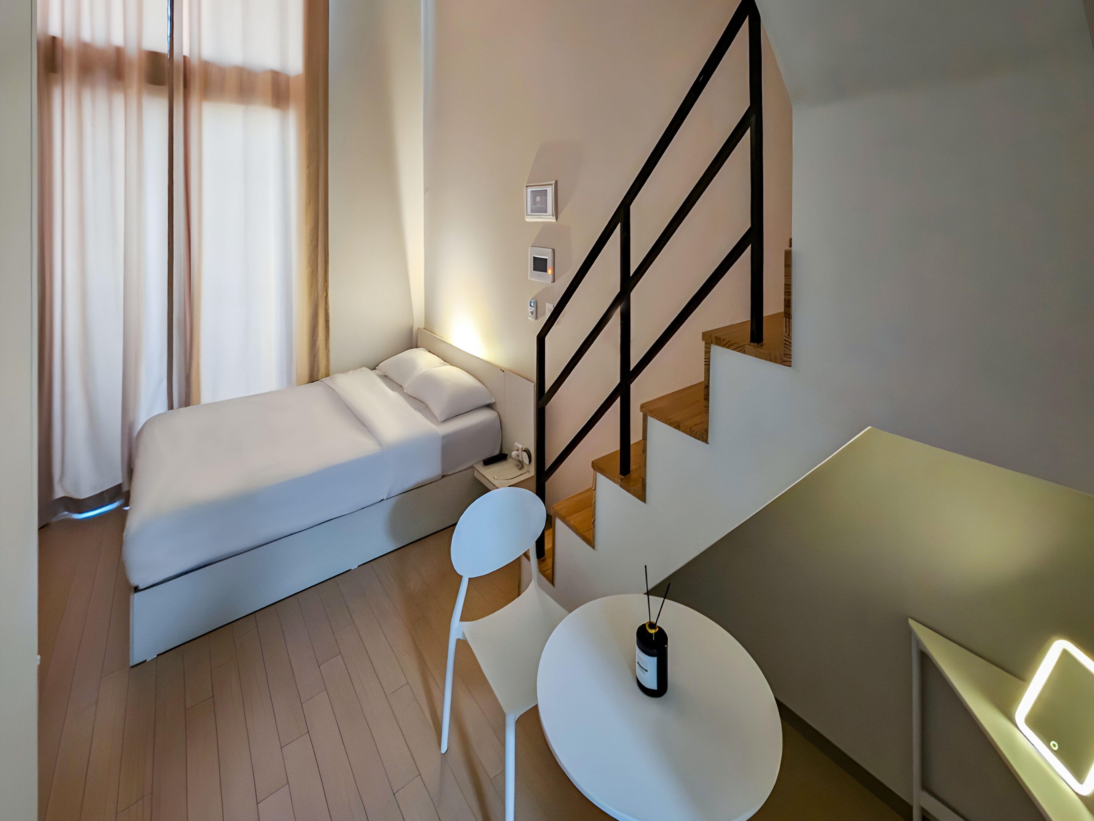 A compact bedroom with a bed, a chair, a small table, and a staircase.