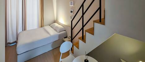 A compact bedroom with a bed, a chair, a small table, and a staircase.
