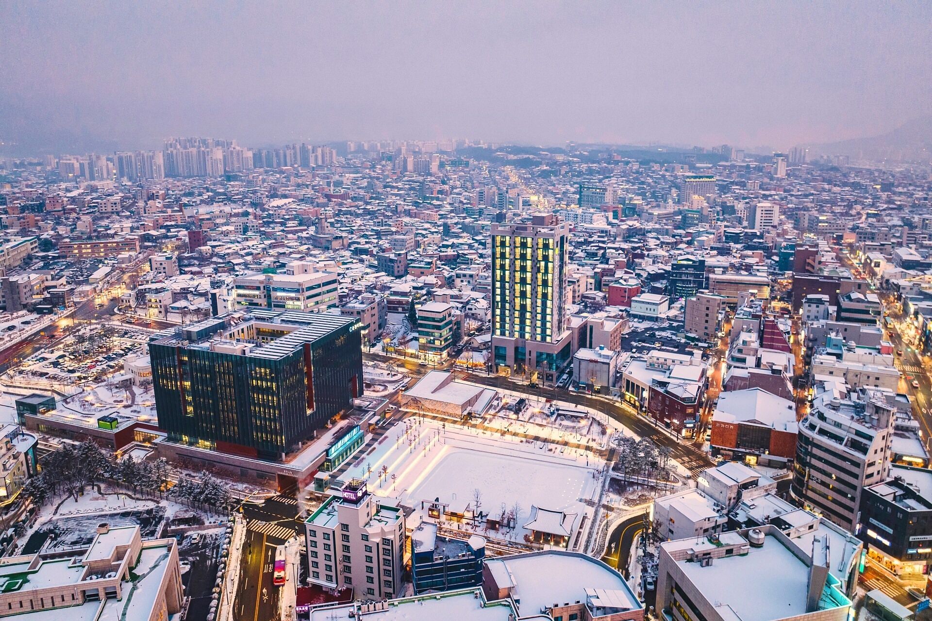 A cityscape with a prominent hotel featuring a modern design, surrounded by other buildings and a snowy environment.