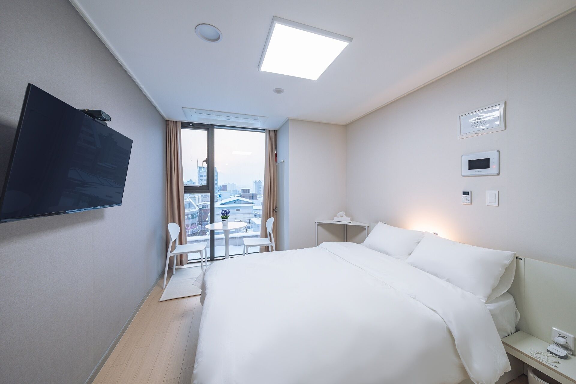 A hotel room with a bed, a desk, a chair, a TV, and a view of the city through the window.