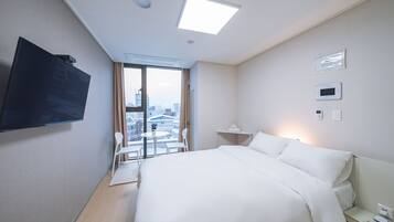 A hotel room with a bed, a desk, a chair, a TV, and a view of the city through the window.