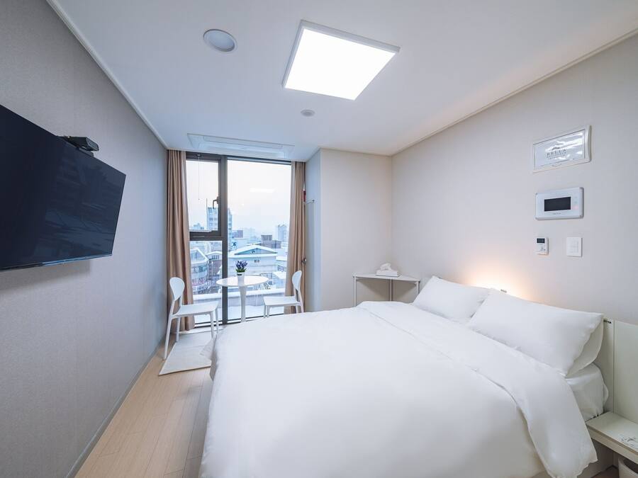A hotel room with a bed, a desk, a chair, a TV, and a view of the city through the window.