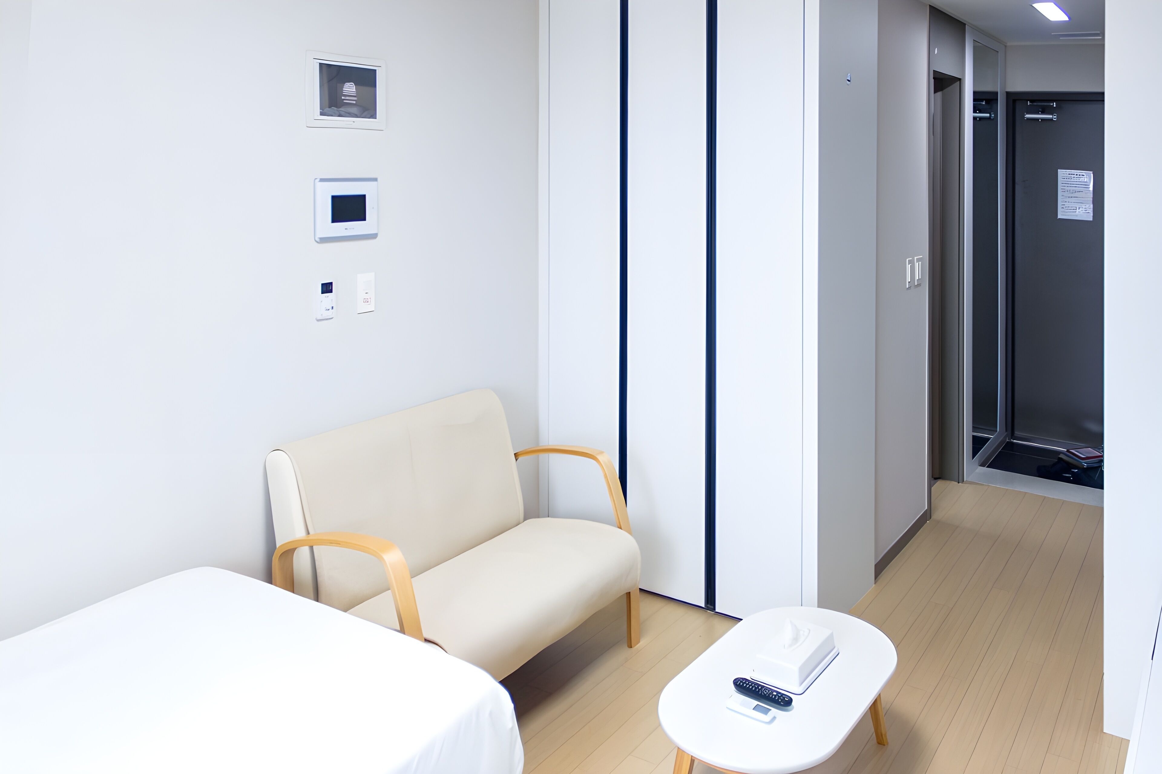 Ett hotellrum med en beige soffa, ett litet vitt bord med en fjärrkontroll och en säng.