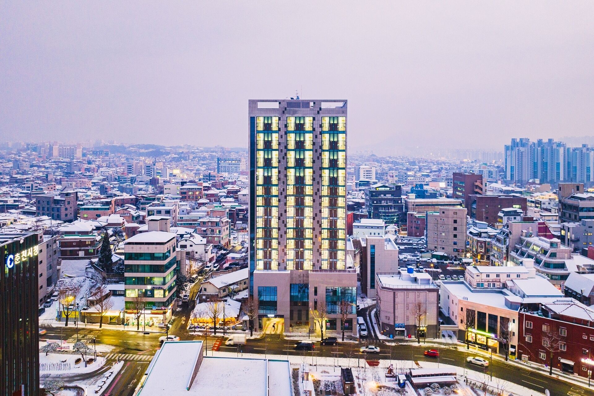 A high-rise building with a grid of windows, surrounded by a cityscape with various buildings and streets.