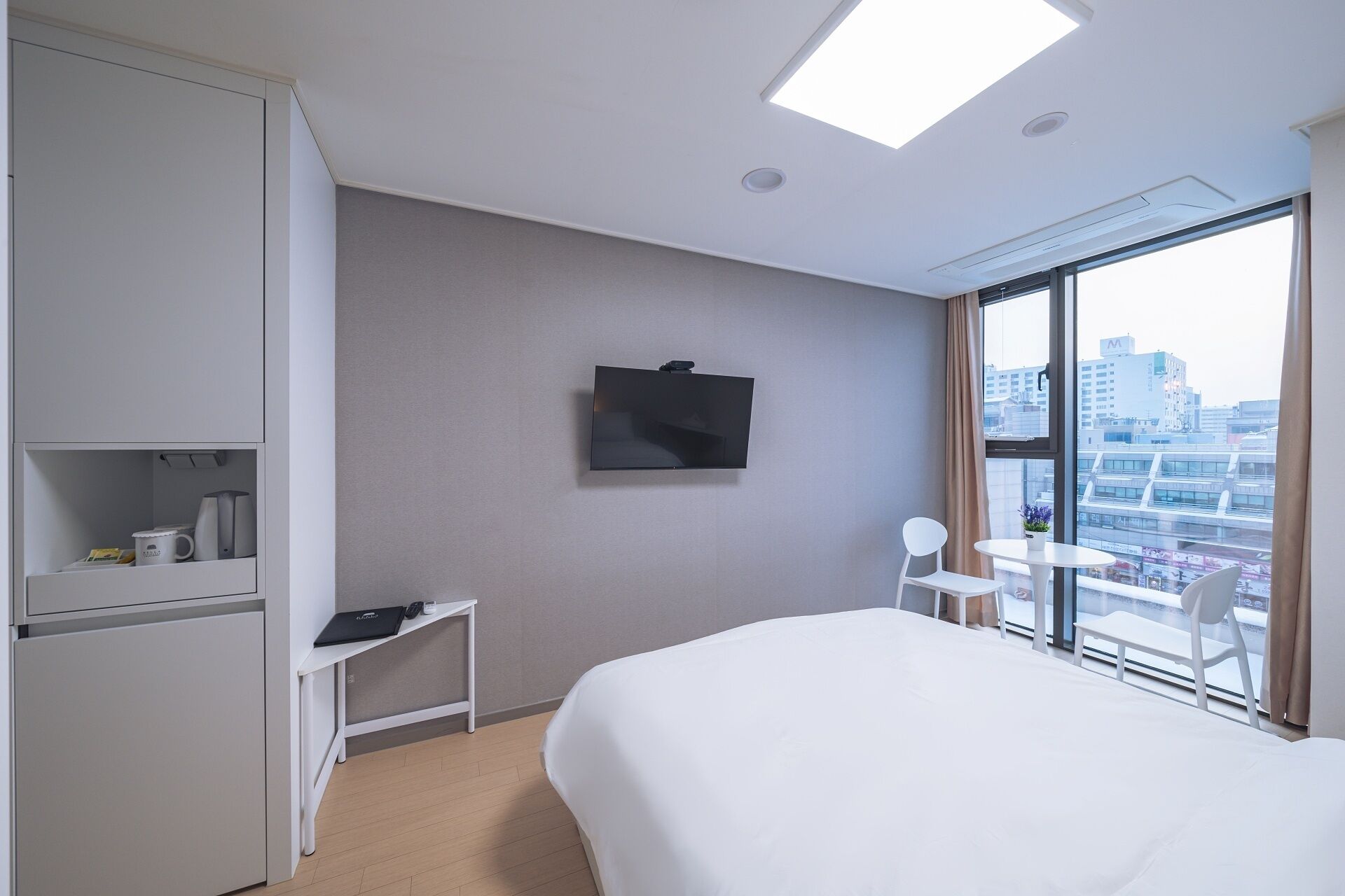 Een hotelkamer met een bed, een bureau, een televisie en een groot raam met uitzicht op de stad.