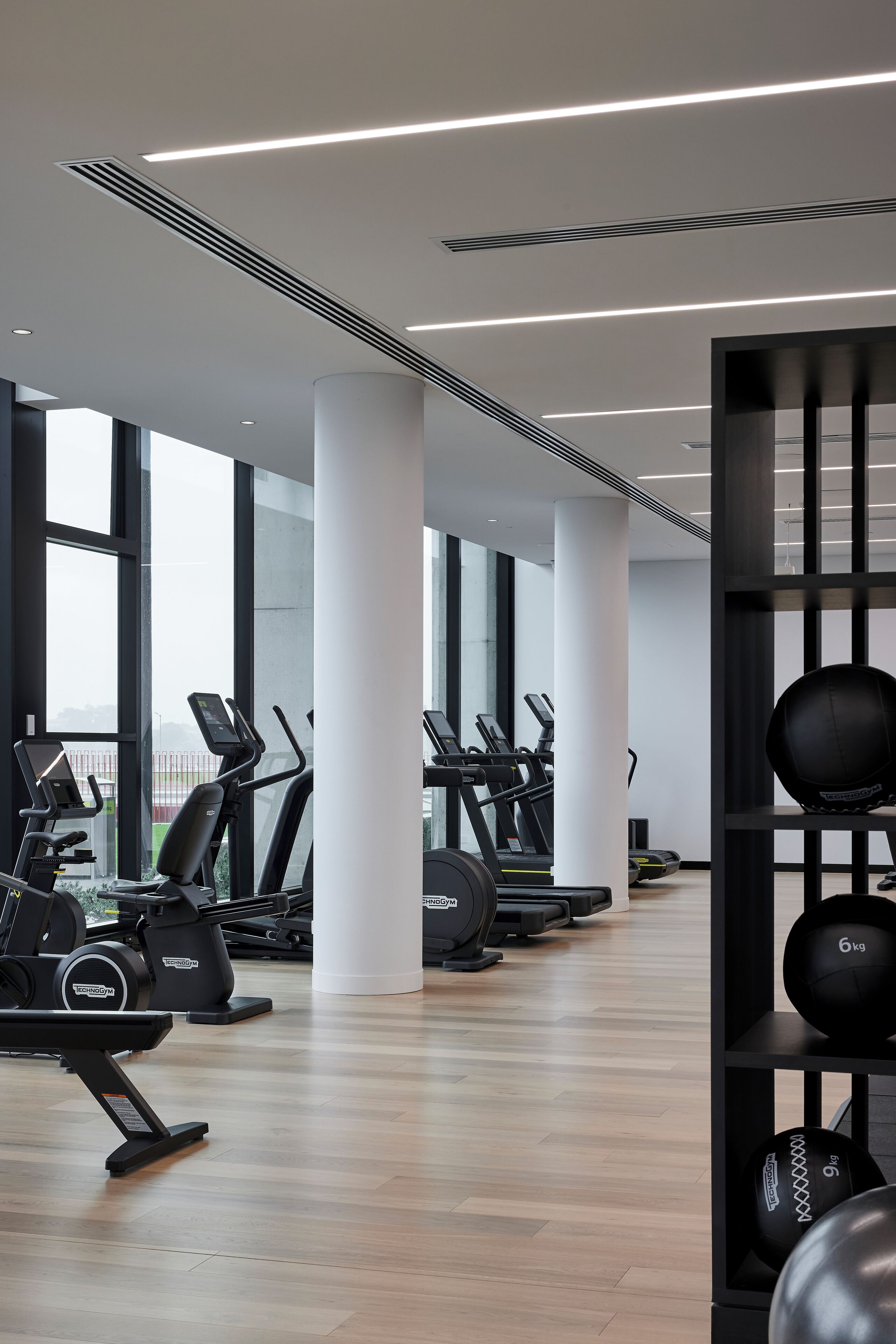A modern gym with cardio machines, weightlifting equipment, and large windows offering views.