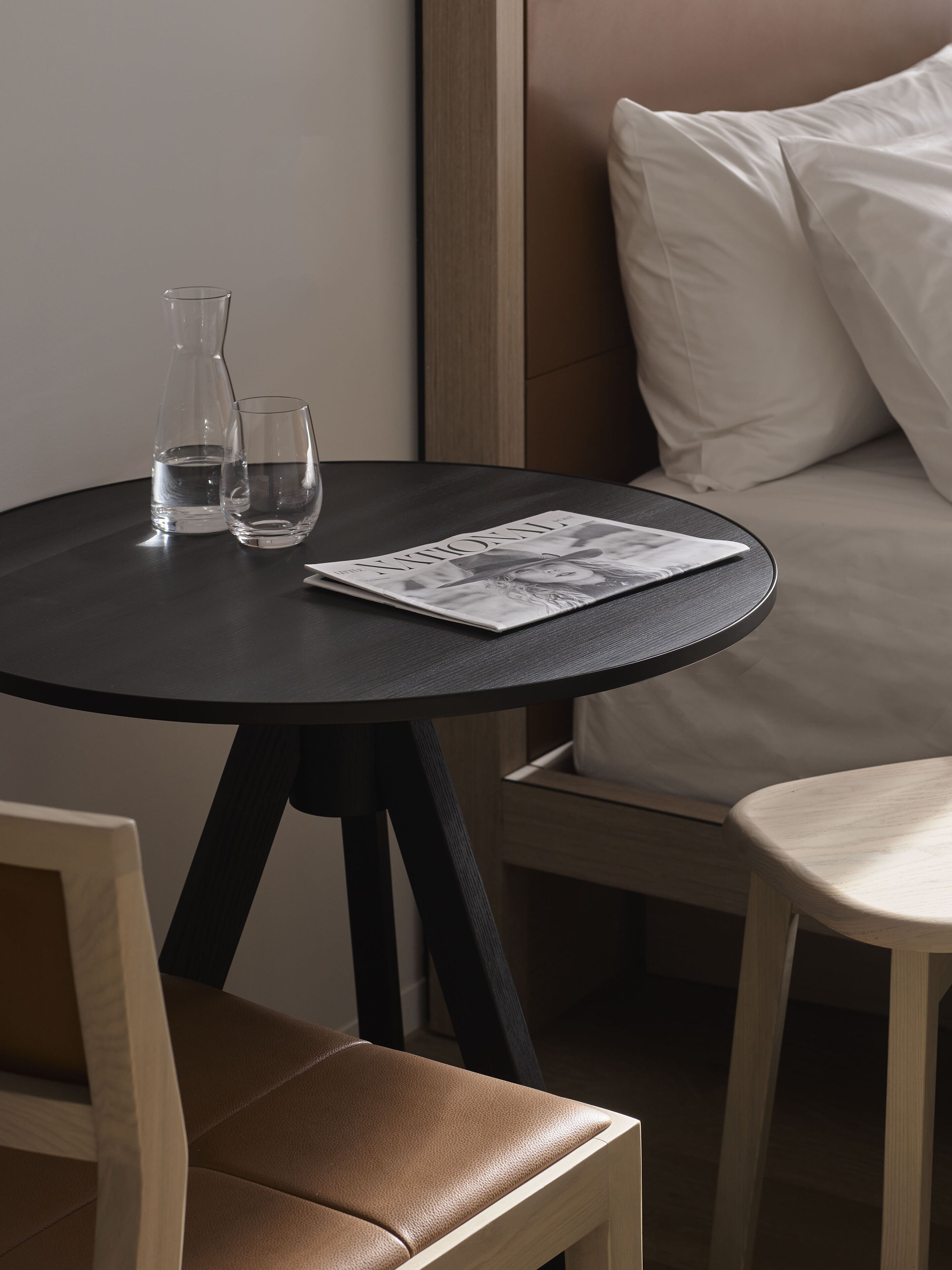 Une petite table ronde avec deux verres et une bouteille, un magazine et un canapé avec des coussins, le tout dans une chambre d’hôtel.