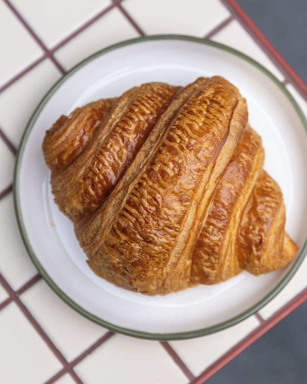 A croissant on a white plate with a grid-patterned tablecloth.