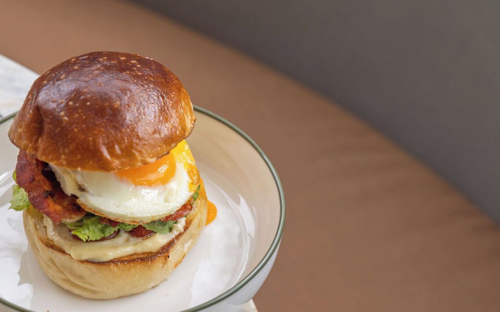 A sandwich with a toasted bun, egg, cheese, lettuce, and bacon, served on a clear glass plate.