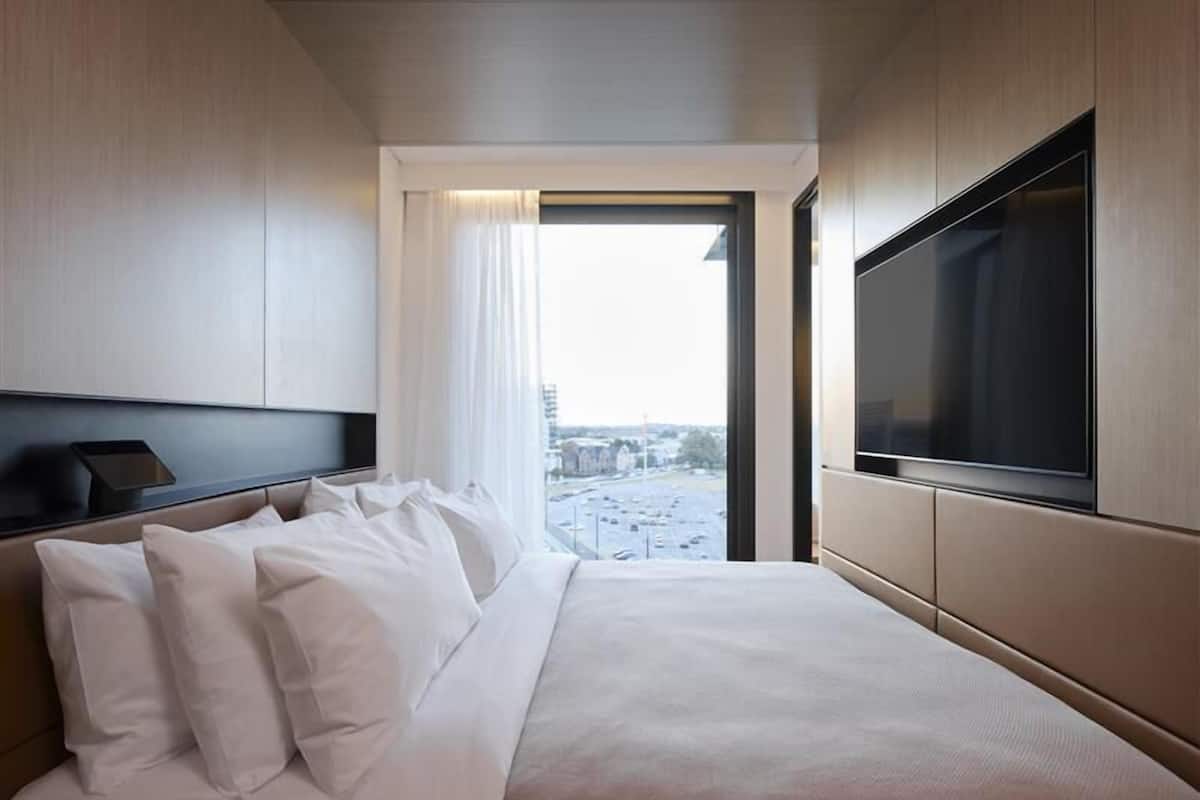 A modern hotel room with a large bed, a flat-screen TV, and a city view through the window.