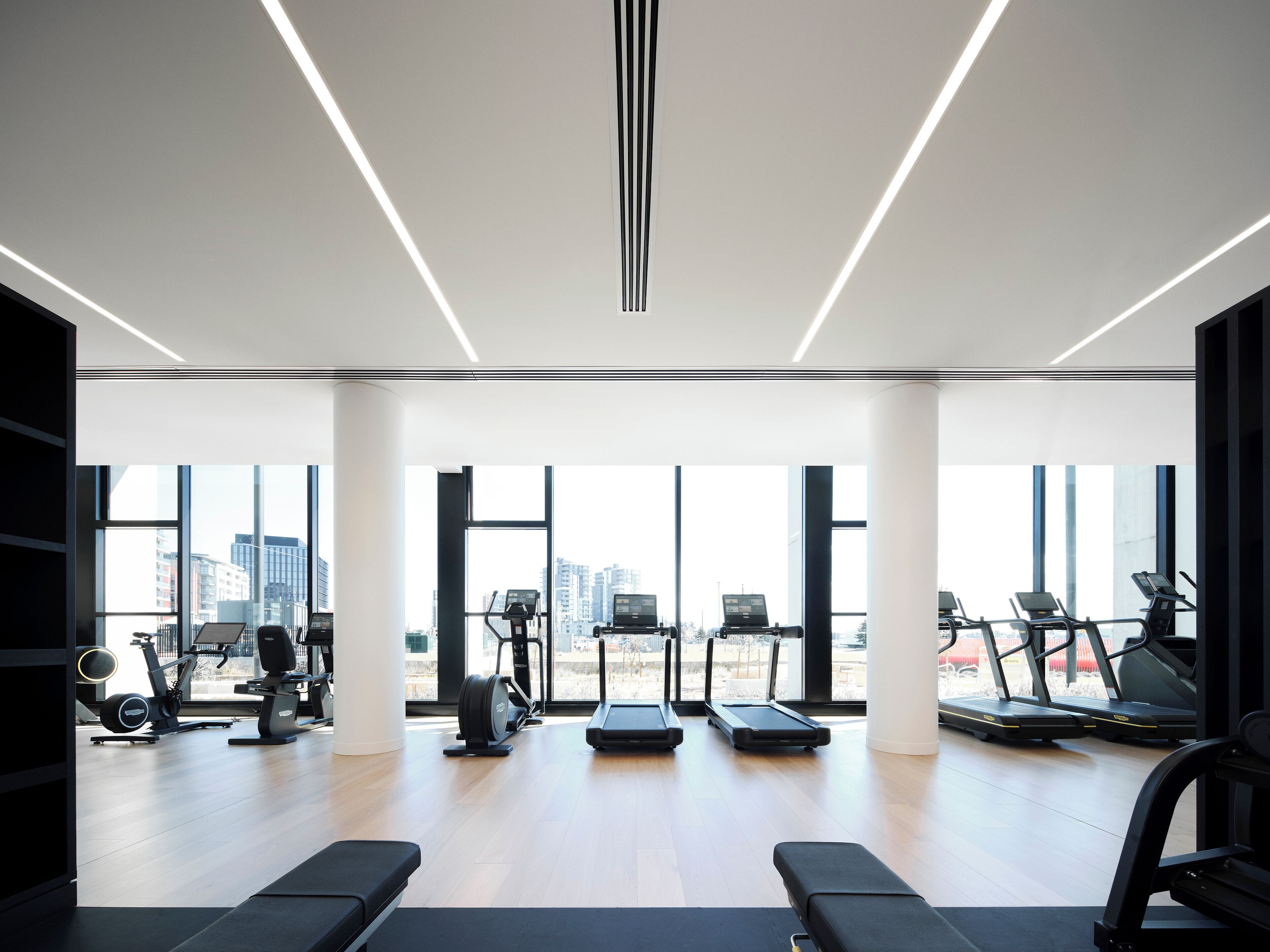 A modern gym with large windows, various exercise equipment, and a city view.