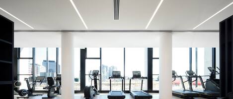 A modern gym with large windows, various exercise equipment, and a city view.