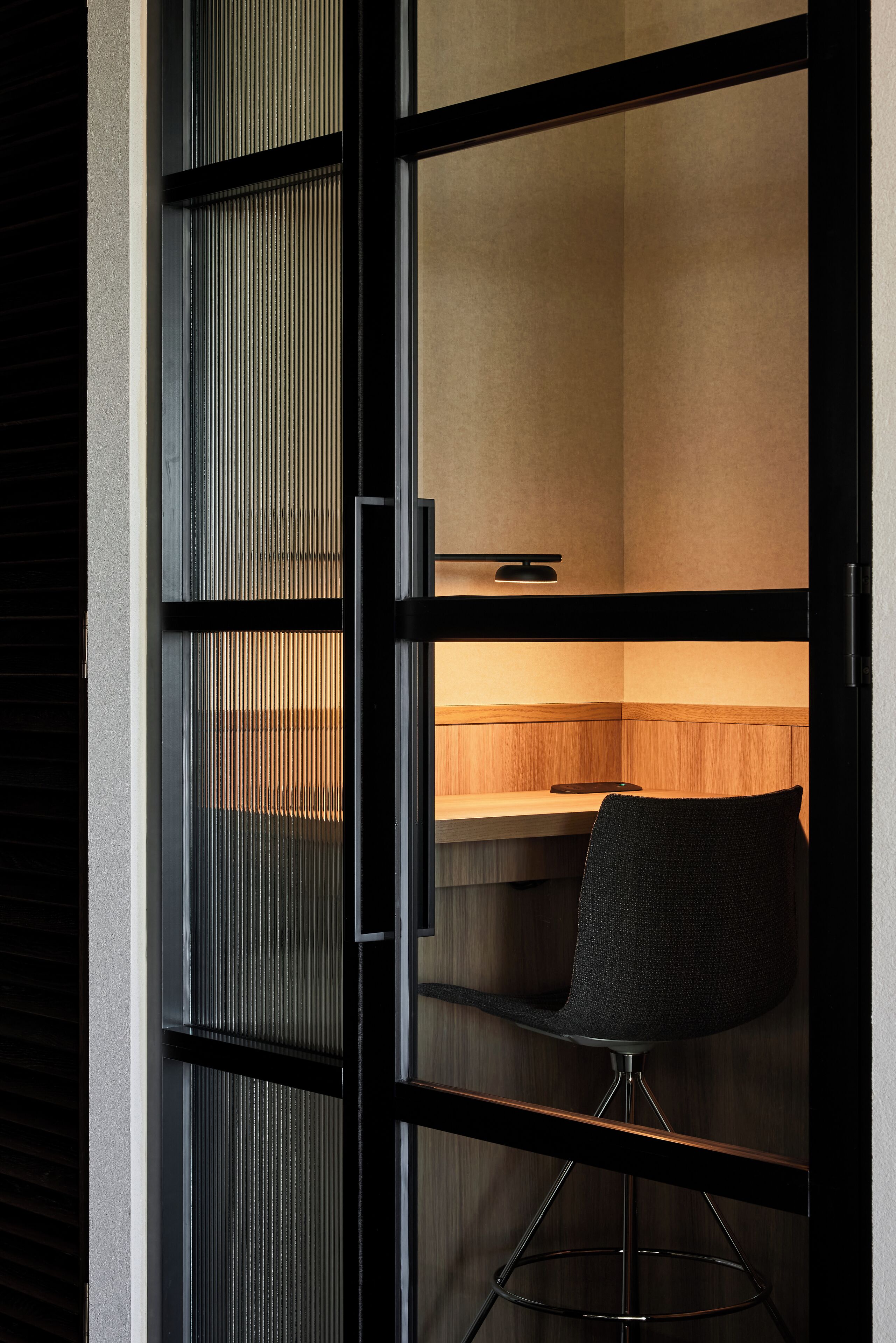 Un interior moderno con una puerta corredera de marco negro, un escritorio de madera y una silla negra.