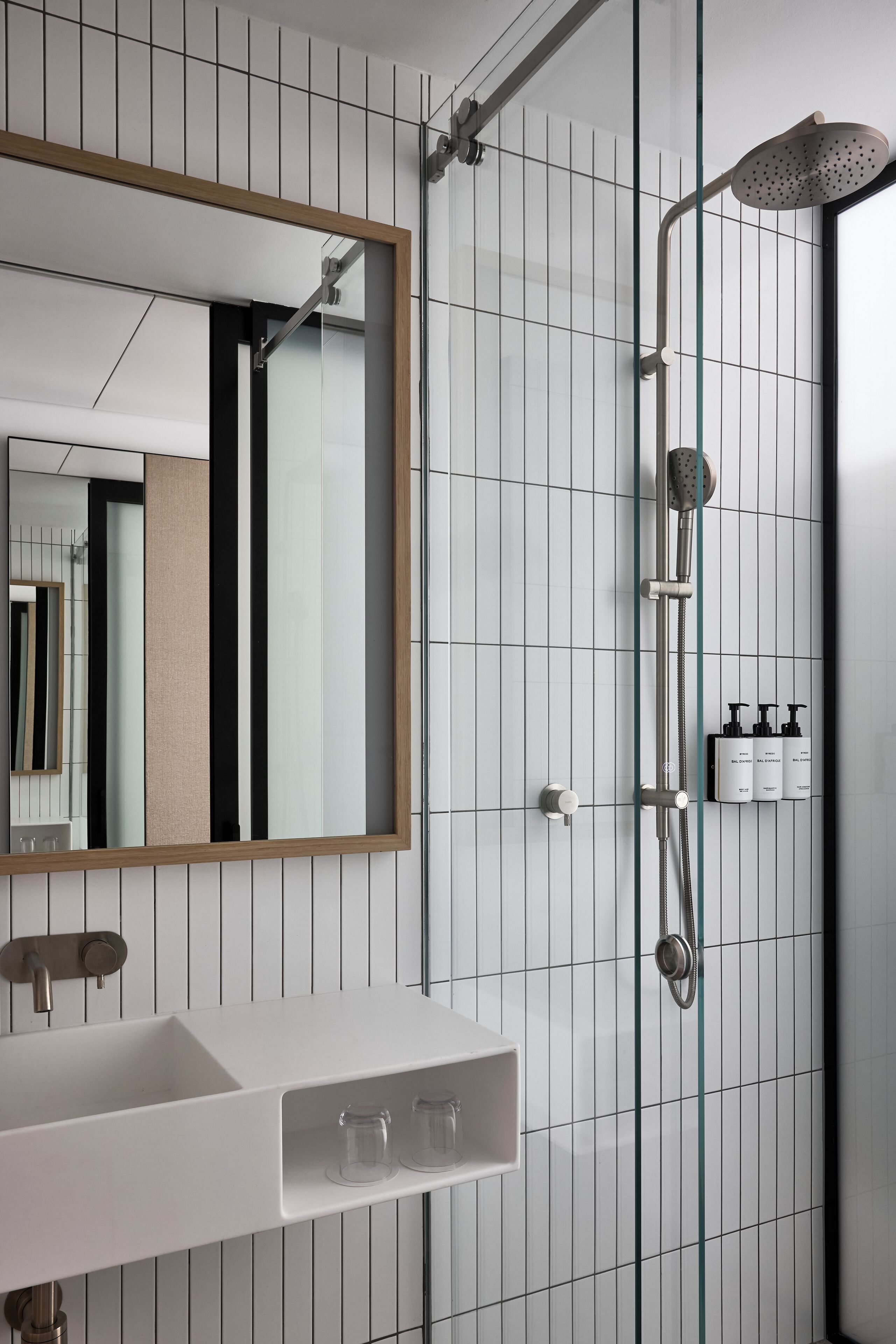 A modern bathroom with a white sink, a large mirror, and a glass-enclosed shower area.