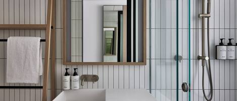 Un baño moderno con un lavamanos blanco, un espejo grande y una ducha con cerramiento de vidrio.