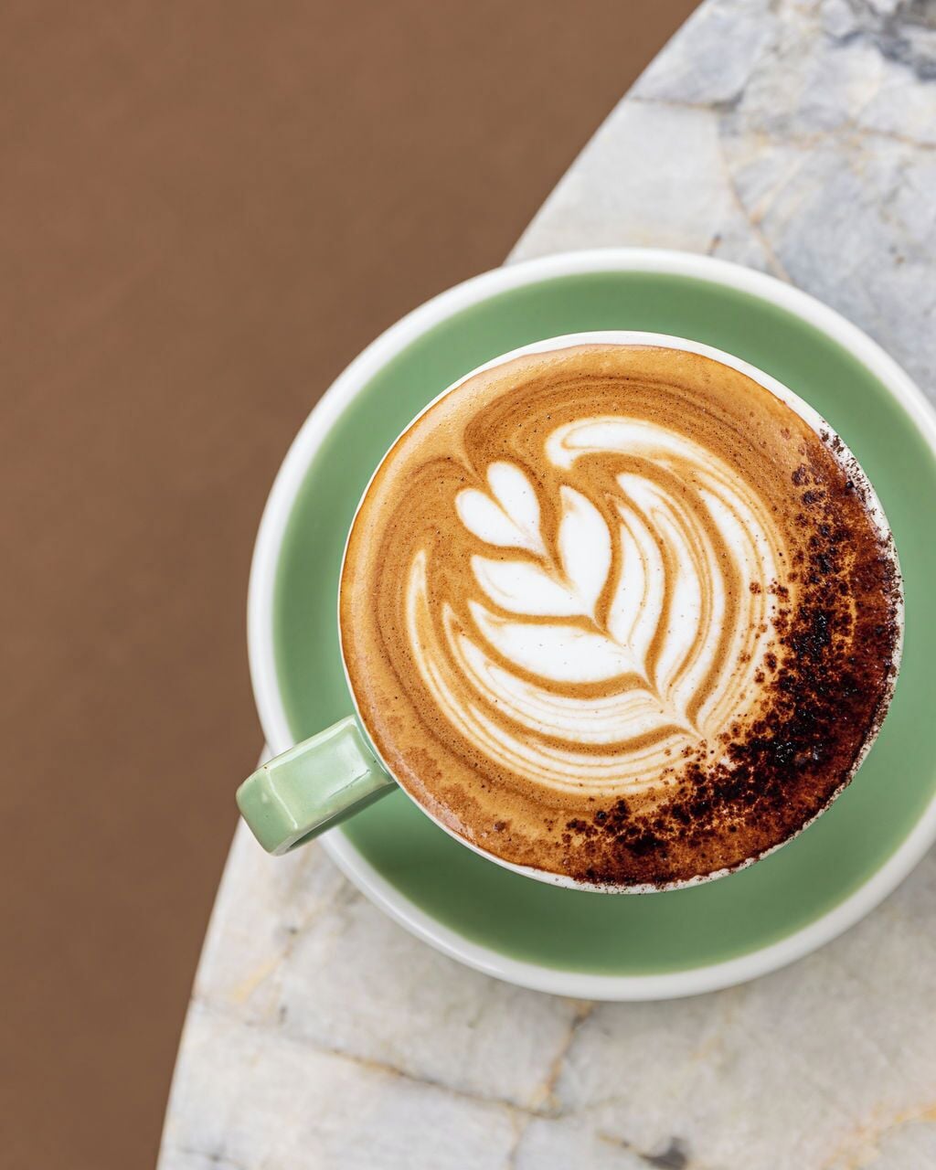 A cup of coffee with latte art on a green saucer.