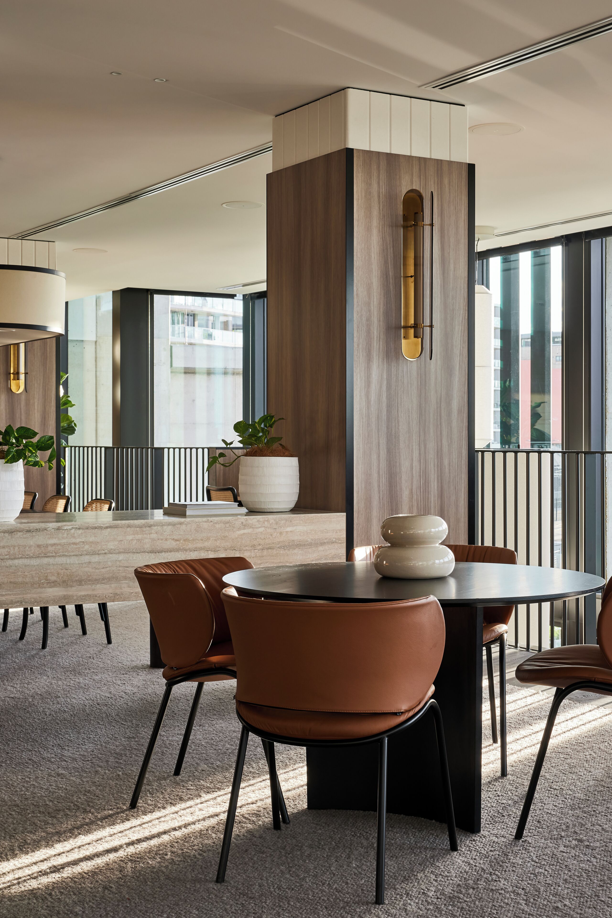 A modern dining area with a round table, brown chairs, and a large potted plant.
