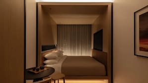 A compact hotel room with a bed, bedside table, chair, and a television.