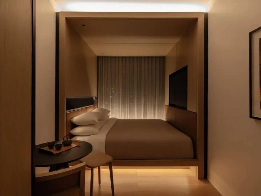 A compact hotel room with a bed, bedside table, chair, and a television.