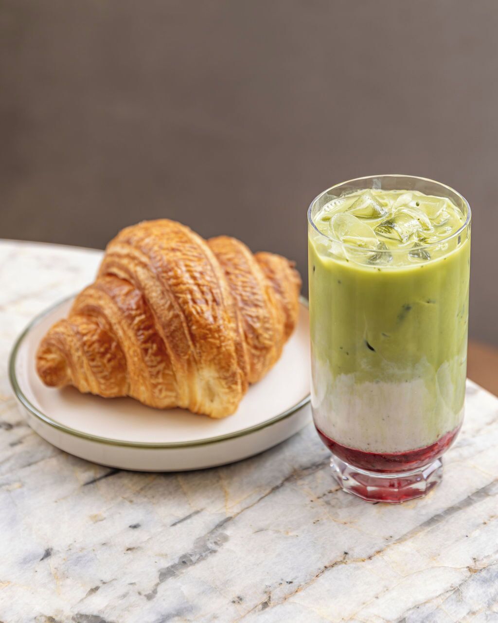 A croissant and a layered beverage on a marble surface.