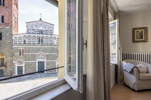 A room with a view of a historic building, a window with curtains, a radiator, and a framed picture on the wall.