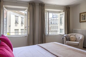 A hotel room with a bed, a chair, and two windows with curtains.