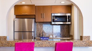 A compact kitchen with a stainless steel refrigerator, a microwave, and wooden cabinets. - Villa del Palmar (Cabo San Lucas)