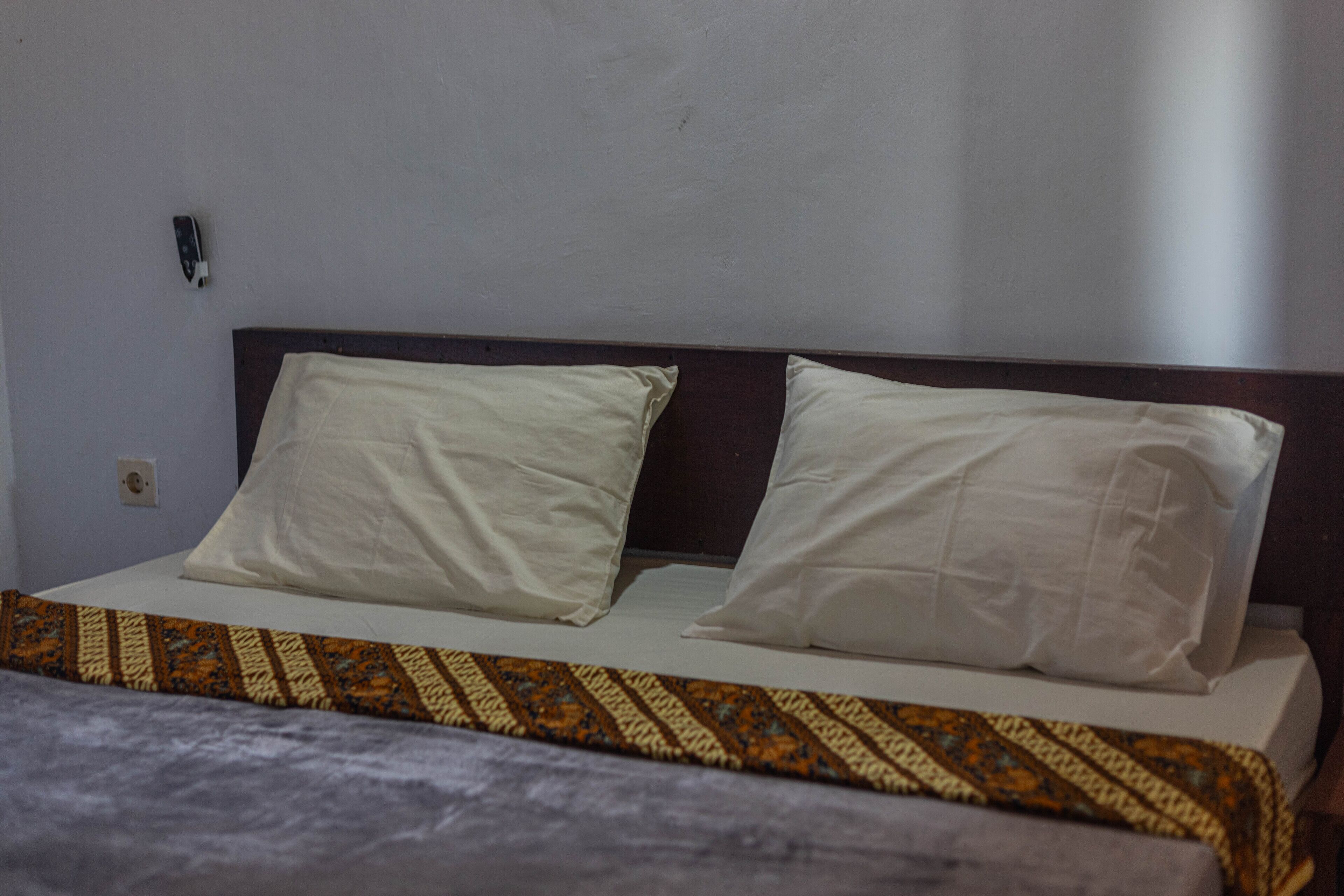 A bed with a patterned bedspread, two pillows, and a wooden headboard.
