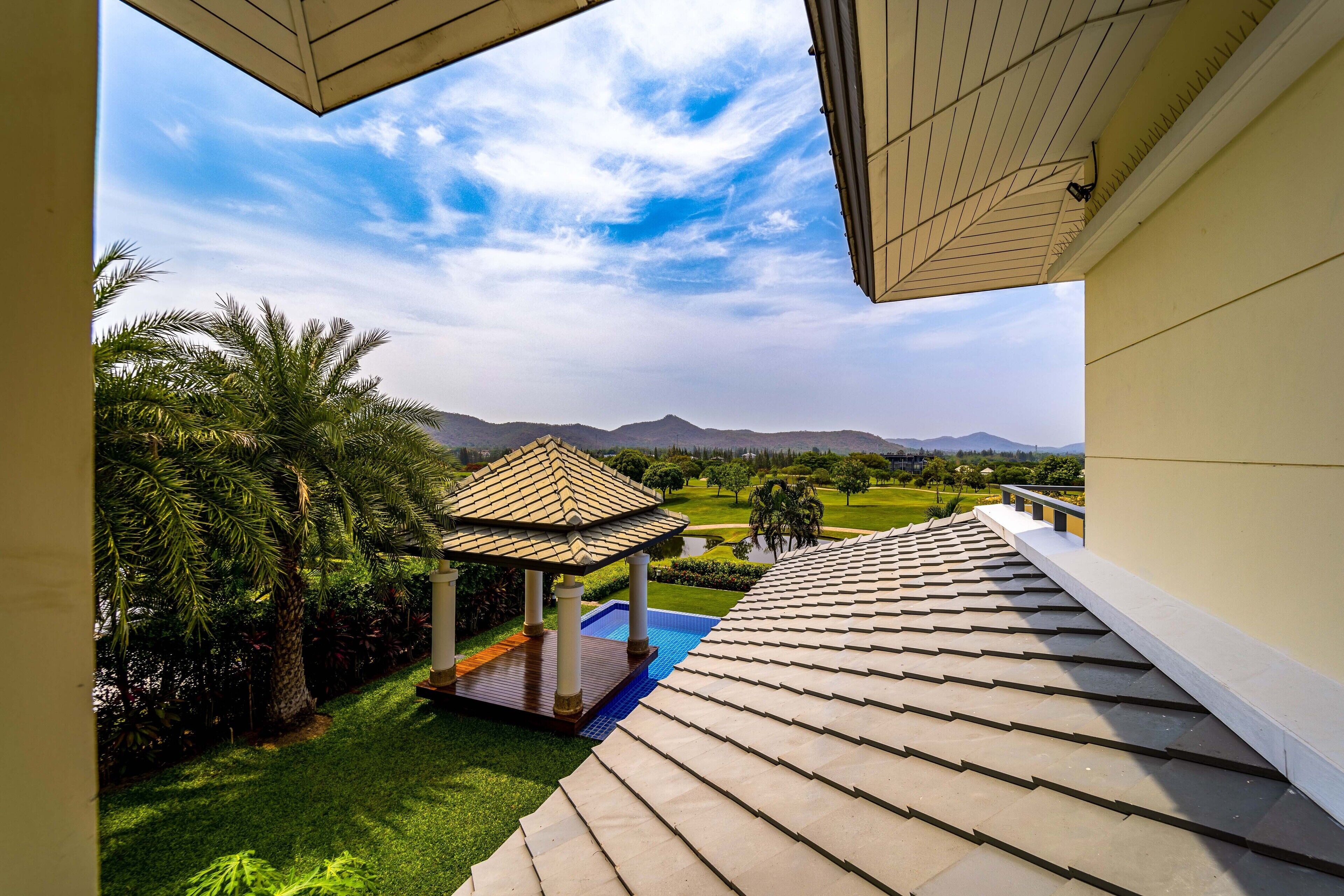 Ein überdachter Außenbereich mit einer Pergola, einem Pool und Blick auf einen angelegten Garten und Berge.