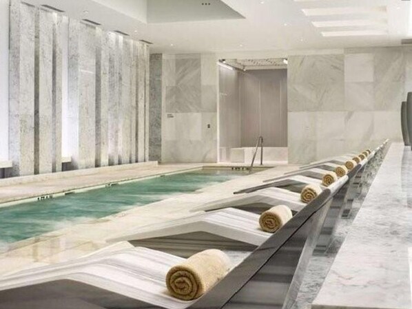 Un moderno espacio de spa con piscina, paredes de mármol y un largo banco con toallas.