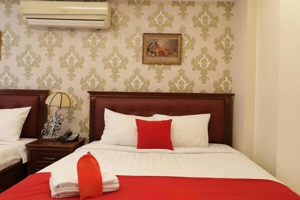 Une chambre d’hôtel avec deux lits, chacun recouvert d’une courtepointe rouge et blanche, dotée d’une tête de lit en bois et d’une petite table de chevet avec une lampe et un téléphone.