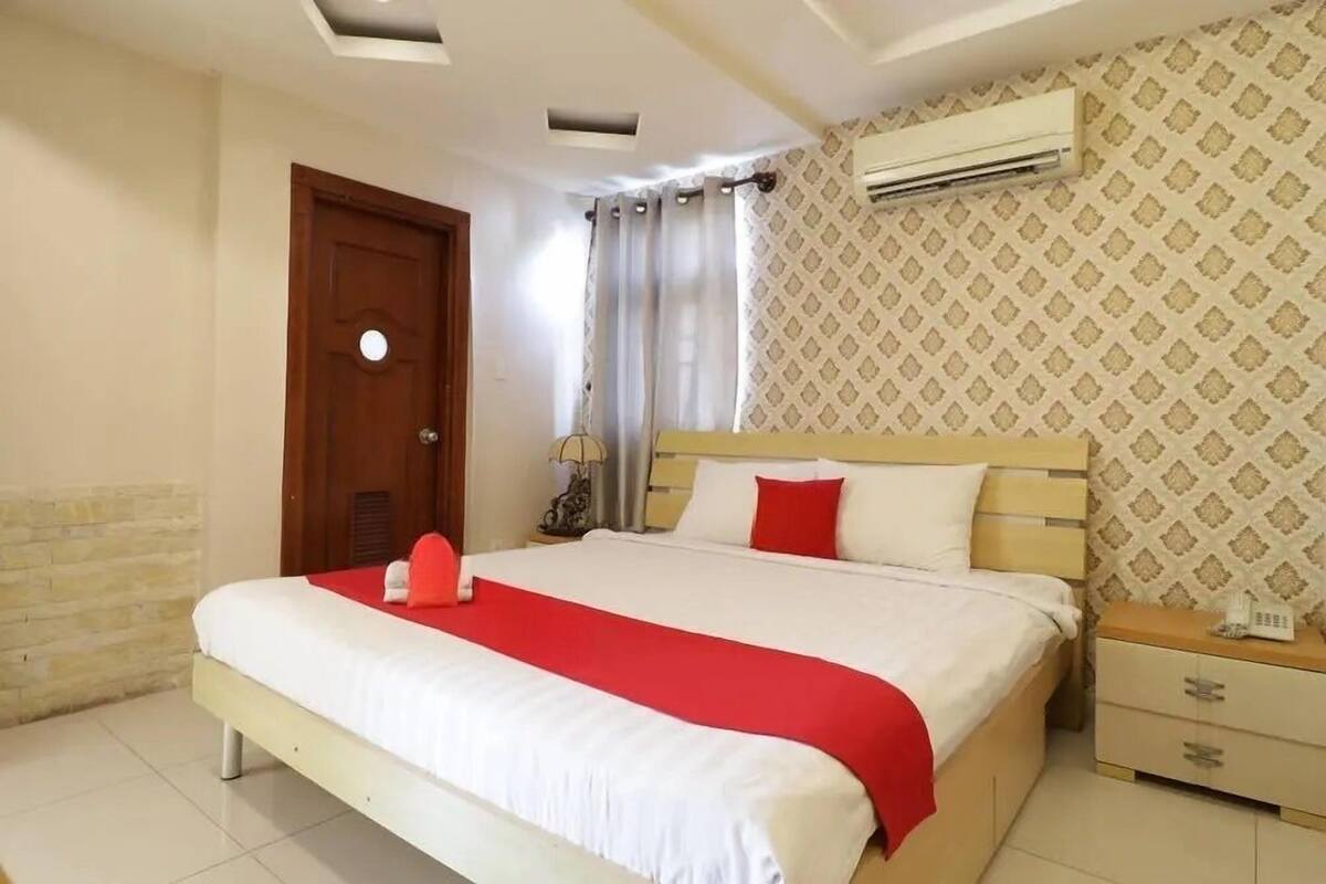 A bedroom with a bed, a nightstand, a lamp, and an air conditioning unit.