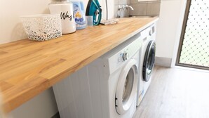 Un espace buanderie moderne comprenant un lave-linge et un sèche-linge, un plan de travail en bois et un panier.