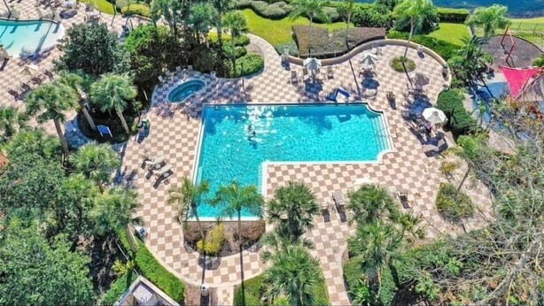 A large pool surrounded by checkered tiles, palm trees, and lounge chairs.
